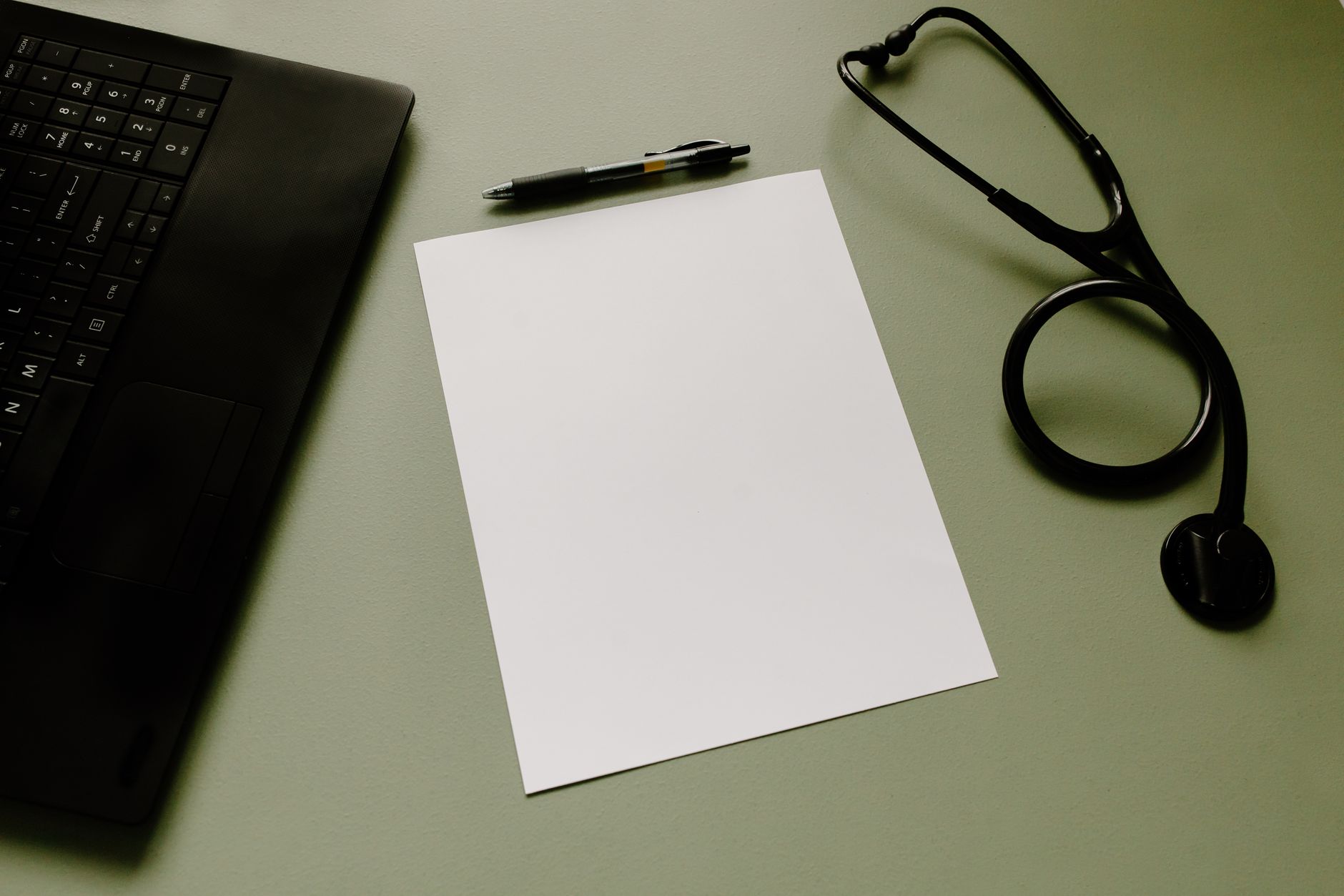 A laptop, stethoscope, pen and paperwork on a desk — the document-driven work of a remote healthcare attorney